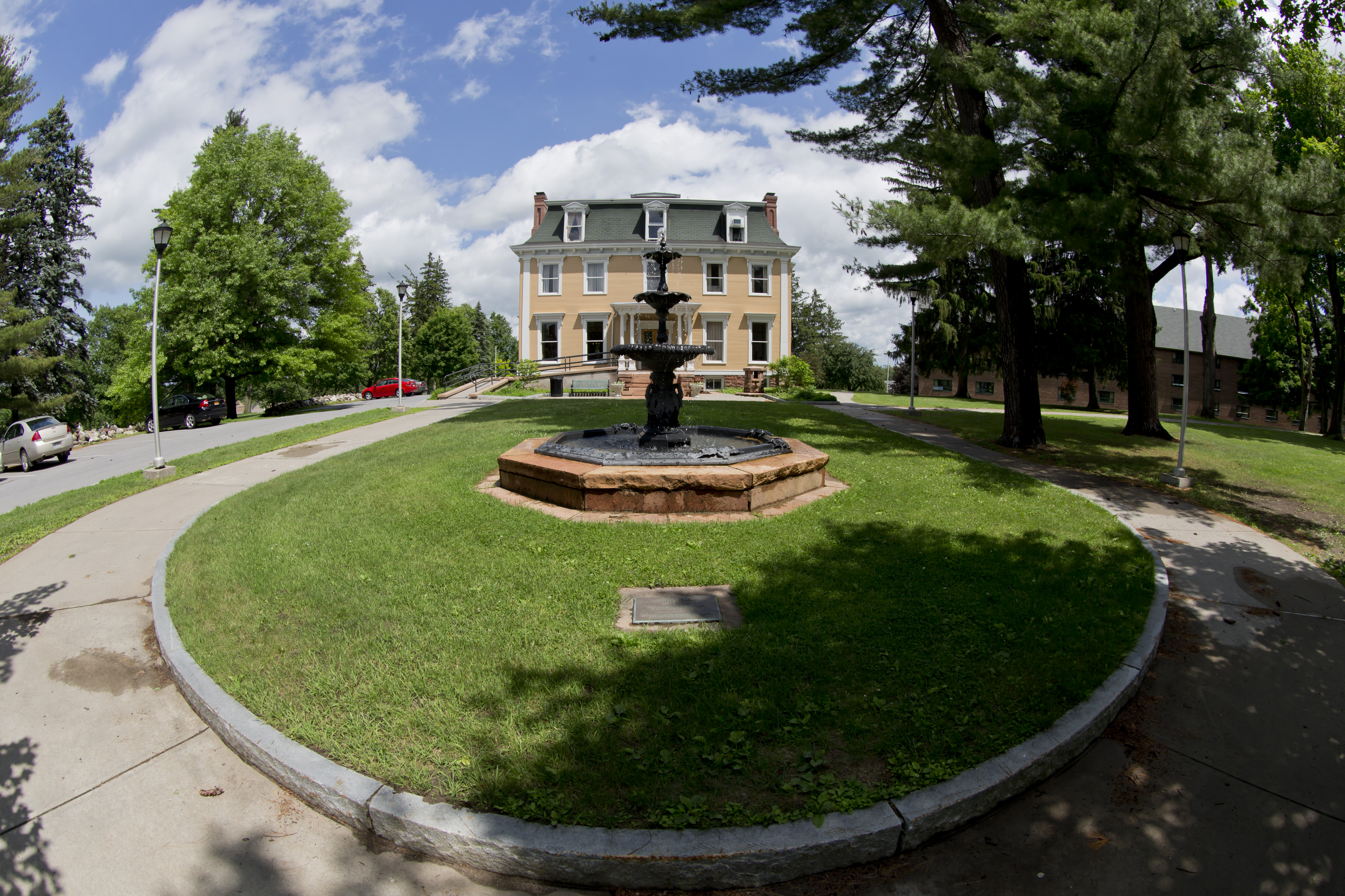 An outdoor photo of Holcroft House, which is home to the office of undergraduate admissions at Clarkson University, and the fountain in front of it.