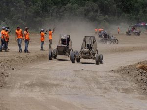 A dirt track with two cars racing and people in orange shirts cheering