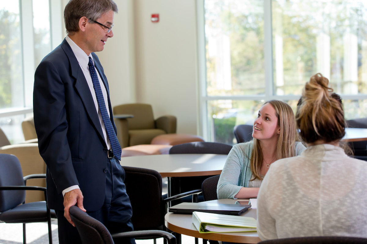 A Graduate School Capital Region Campus faculty member talks with two students in the atrium during a study session.