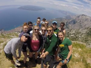A group of people wearing clarkson university t-shirts taking a selfie while standing on a cliff