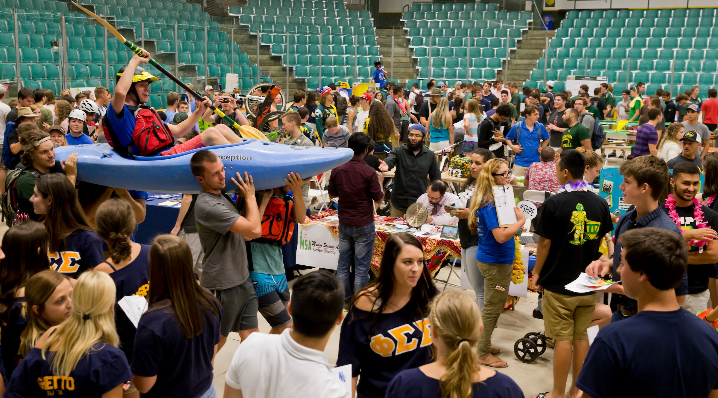 Several students carry another student in a kayak through a crowd of dozens of students at the Student Activities Fair.