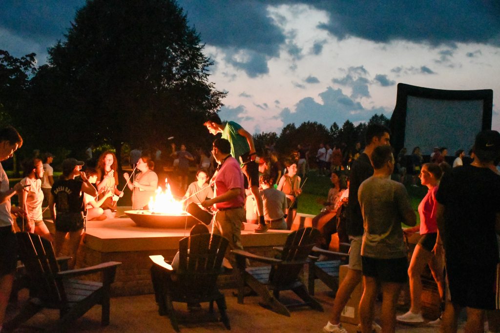 Several Clarkson students gather outside and in front of an outdoor fire pit during an ice breaker event for transfer students.