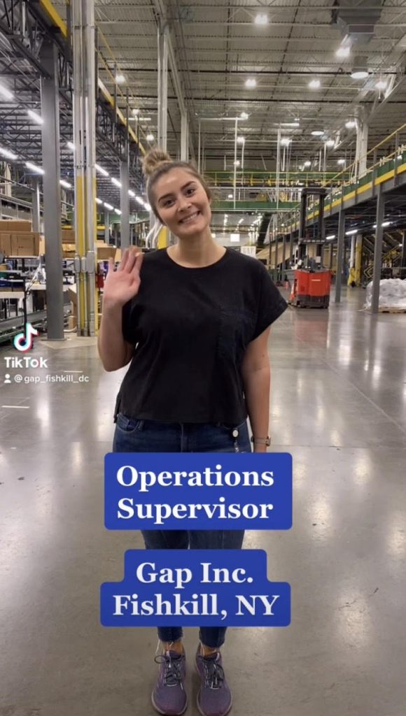 A women standing smiling waving at the camera with the words Operations Supervisor Gap Inc. FishKill, NY on the image