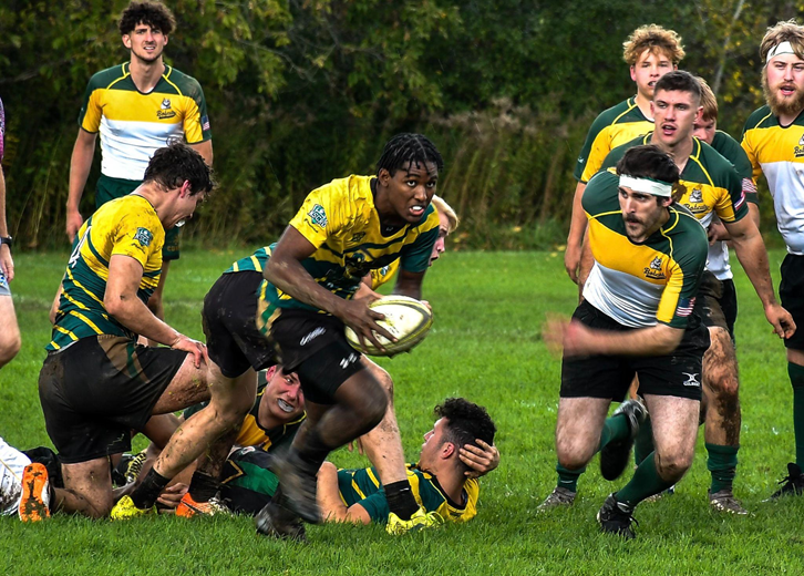 A group of men playing rugby in white, yellow, and green uniforms 