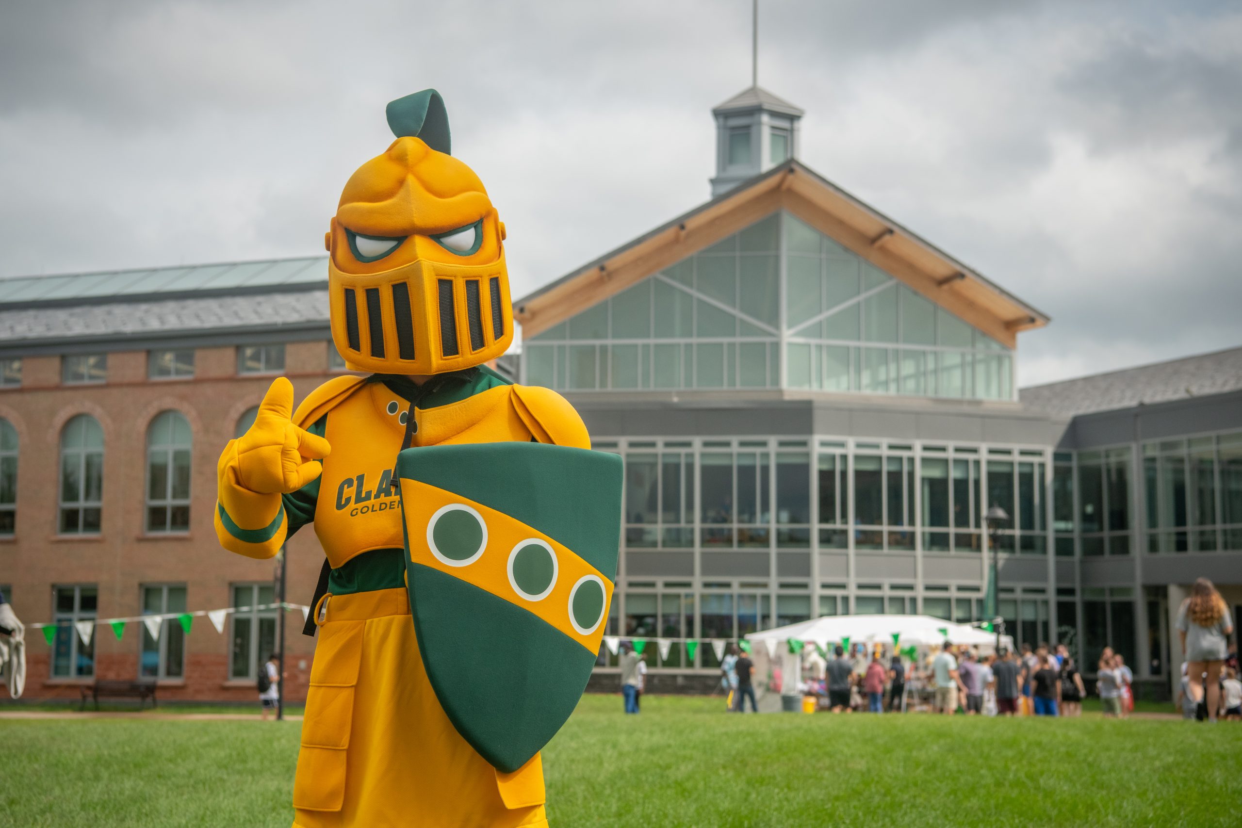 The Golden Knight with a thumbs up standing on cheel lawn with the student center in the background