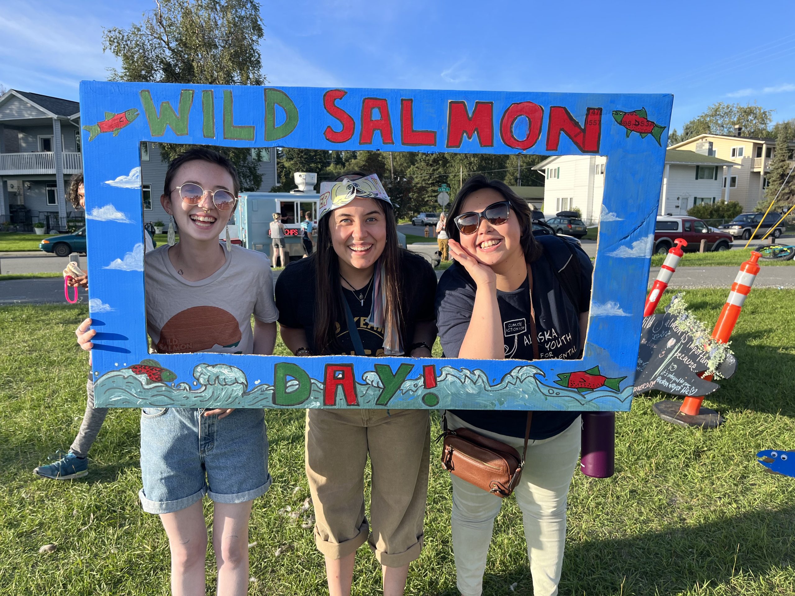 Three people with their heads sticking out of a square photo frame cut out with the words Salmon hand painted on it.