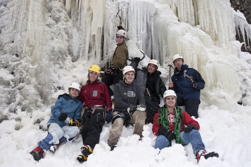 A group of students in front of a mountain of ice. They are all in ice climbing gear