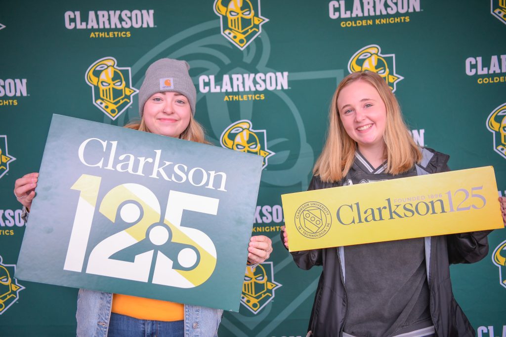 Two women holding up signs. The women on the left is holding a sign that says Clarkson 125 and the one on the right is holding a sign with the logo that reads Clarkson 125 Founded 1896